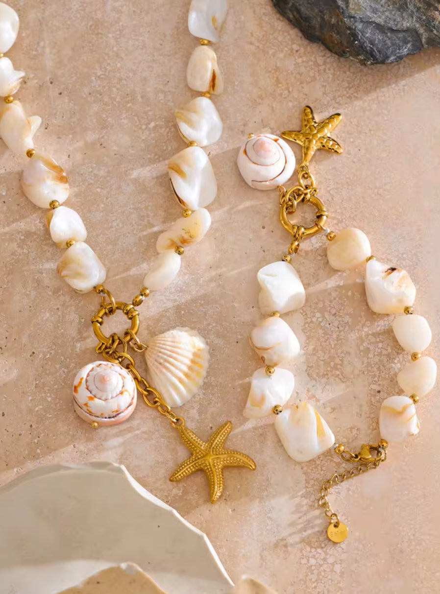 Necklace with shell and starfish charms on a sandy background. A woman wearing a bold statement necklace with a chunky gold chain.