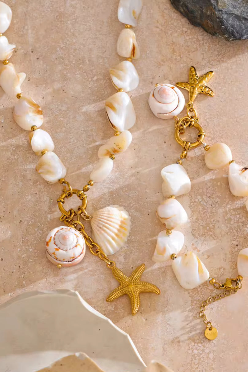 Necklace with shell and starfish charms on a sandy background. A woman wearing a bold statement necklace with a chunky gold chain.