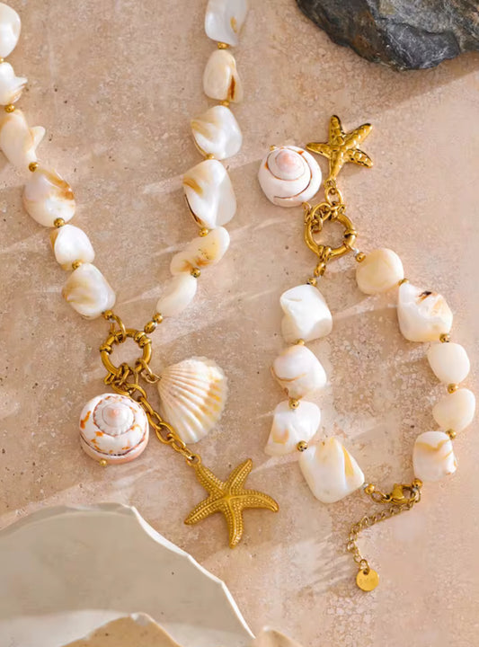 Necklace with shell and starfish charms on a sandy background. A woman wearing a bold statement necklace with a chunky gold chain.